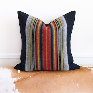 May include: A black and grey striped throw pillow with red, yellow, and blue accents. The pillow is made of a soft, textured fabric.