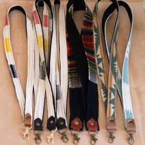 May include: Six colorful woven lanyards with black edging and gold metal clasps. The lanyards have different patterns and colors, including red, blue, green, yellow, and white.