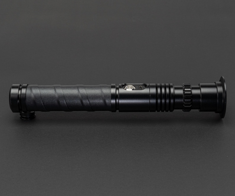 May include: A black lightsaber prop with a textured grip and a silver button. The lightsaber has a black metal barrel and a black plastic end cap.