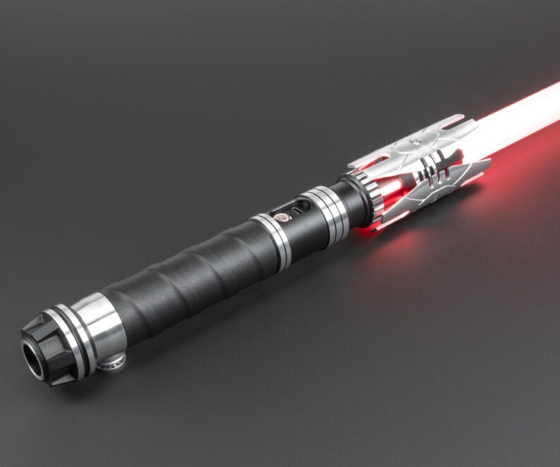 May include: A black lightsaber with a silver handle and a red blade. The lightsaber has a textured grip and a silver emitter.