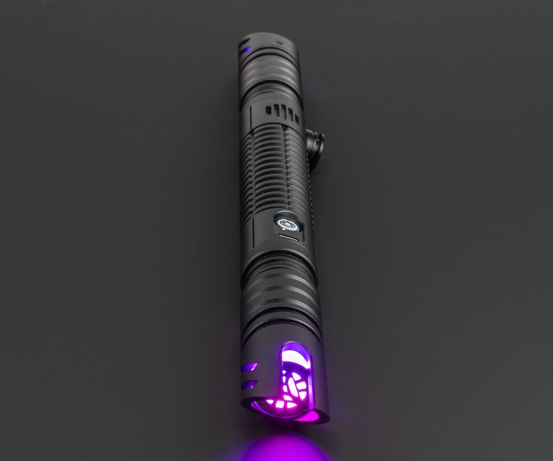May include: A black lightsaber with a purple light saber blade. The lightsaber has a textured black handle with a button on the side.