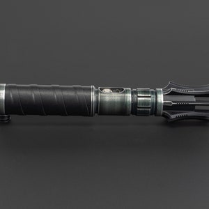 K&ouml;nnte beinhalten: Ein schwarzes und silbernes Lichtschwert mit einem strukturierten Griff und einer einzigartigen, mehrzackigen Klinge. Die Klinge ist mit scharfen Spitzen und einer gezackten Kante gestaltet.