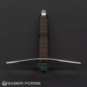 Op de afbeelding: Een zilveren lightsaber met een bruine leren greep en een groene gloeiende punt.