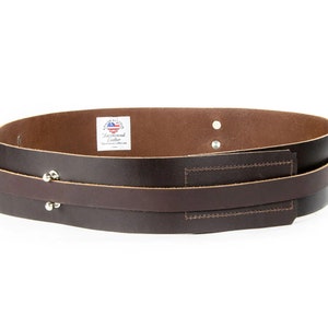 May include: A brown leather belt with two straps and silver rivets. The belt has a small label that says "Backwood Leather".