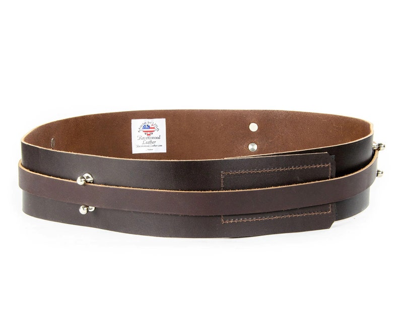 May include: A brown leather belt with two straps and silver rivets. The belt has a small label that says "Backwood Leather".