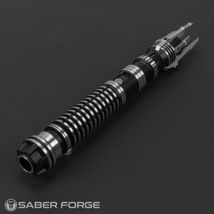 Puede incluir: Un sable de luz negro y plateado con un agarre texturizado y un emisor plateado. El sable de luz tiene un dise&ntilde;o &uacute;nico con un emisor en forma de garra.