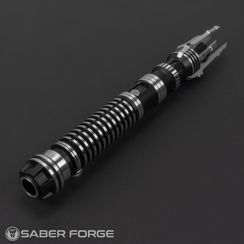 Puede incluir: Un sable de luz negro y plateado con un agarre texturizado y un emisor plateado. El sable de luz tiene un dise&ntilde;o &uacute;nico con un emisor en forma de garra.