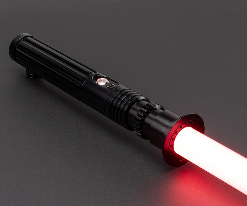 Op de afbeelding: Een zwart lightsaber met een rode blade. De lightsaber heeft een getextureerde handgreep en een zwarte emitter.