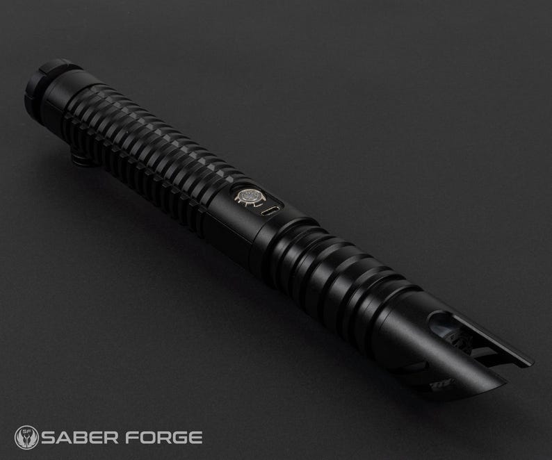 May include: A black lightsaber with a ribbed handle and a detailed emitter. The lightsaber has a button with a logo and is set against a dark background. The Saber Forge logo is visible at the bottom.