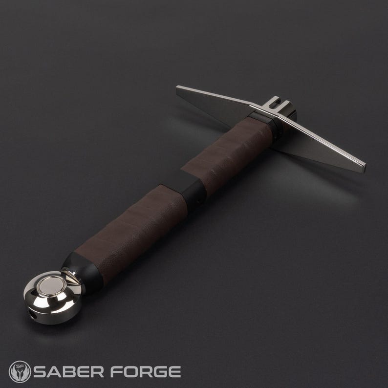 May include: A cross-guard lightsaber hilt featuring a brown leather-wrapped grip, a polished silver-tone pommel, and a metallic cross-guard emitter. The hilt includes black accents and a sleek, cylindrical design with a Saber Forge logo at the bottom.