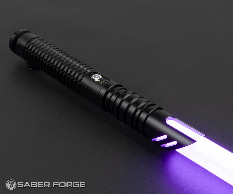 May include: A black lightsaber with a ribbed handle and a glowing purple blade. The lightsaber has a sleek design with a button and a logo that says "Saber Forge" at the bottom.