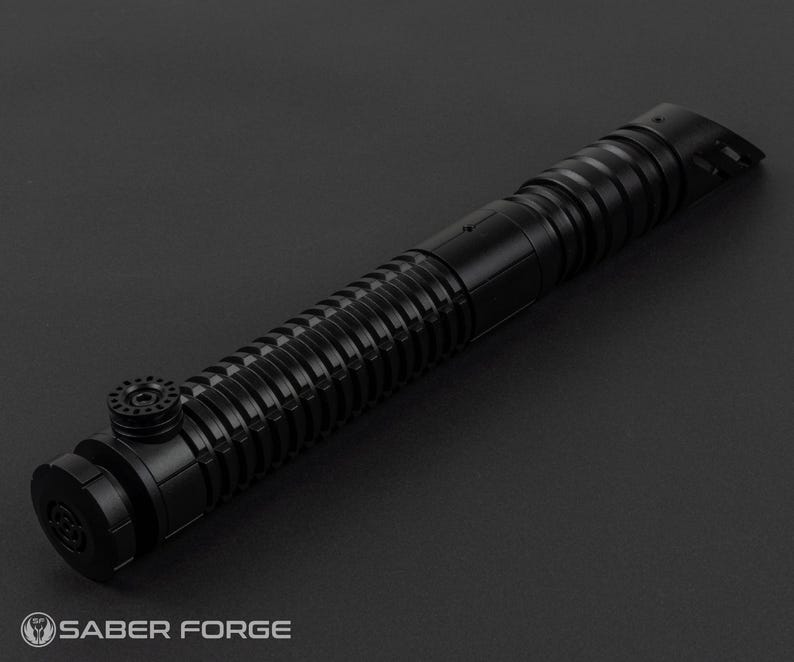 May include: A black lightsaber hilt with a ribbed design and various circular and cylindrical components. The hilt has a textured grip and a pommel with a circular design. The Saber Forge logo is visible at the bottom.