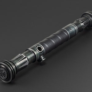 Pode incluir: Um sabre de luz preto e prateado com uma pega texturizada e um emissor circular. O sabre de luz tem um acabamento met&aacute;lico verde escuro.