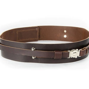 May include: A brown leather belt with a silver buckle and metal studs. The belt is double layered and has a strap that can be adjusted.