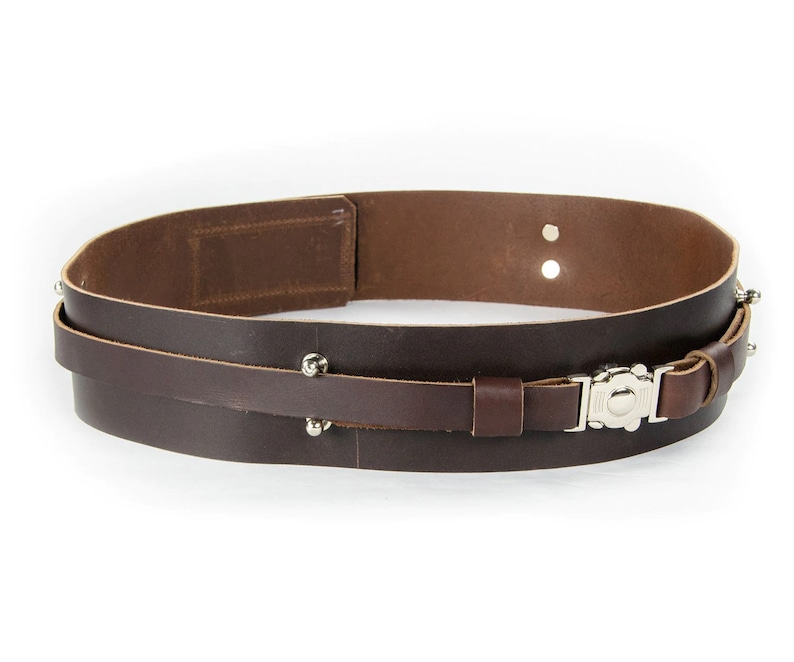 May include: A brown leather belt with a silver buckle and metal studs. The belt is double layered and has a strap that can be adjusted.