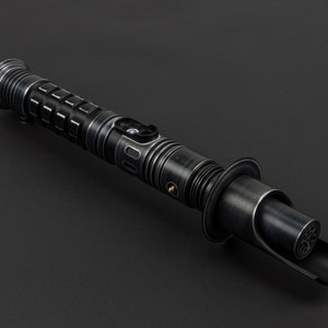 K&ouml;nnte beinhalten: Ein schwarzes Lichtschwert mit silbernen und goldenen Akzenten. Das Lichtschwert hat einen strukturierten Griff und eine schwarze Klinge.