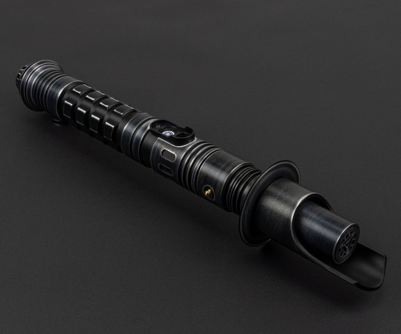 K&ouml;nnte beinhalten: Ein schwarzes Lichtschwert mit silbernen und goldenen Akzenten. Das Lichtschwert hat einen strukturierten Griff und eine schwarze Klinge.