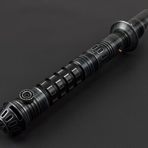 K&ouml;nnte beinhalten: Ein schwarzes Lichtschwert mit einem silbernen Griff und einem strukturierten Griff. Das Lichtschwert hat eine schwarze Klinge und eine silberne Spitze.