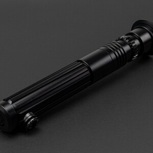 Op de afbeelding: Een zwart lightsaber-accessoire met een getextureerde handgreep en een zwarte kling.