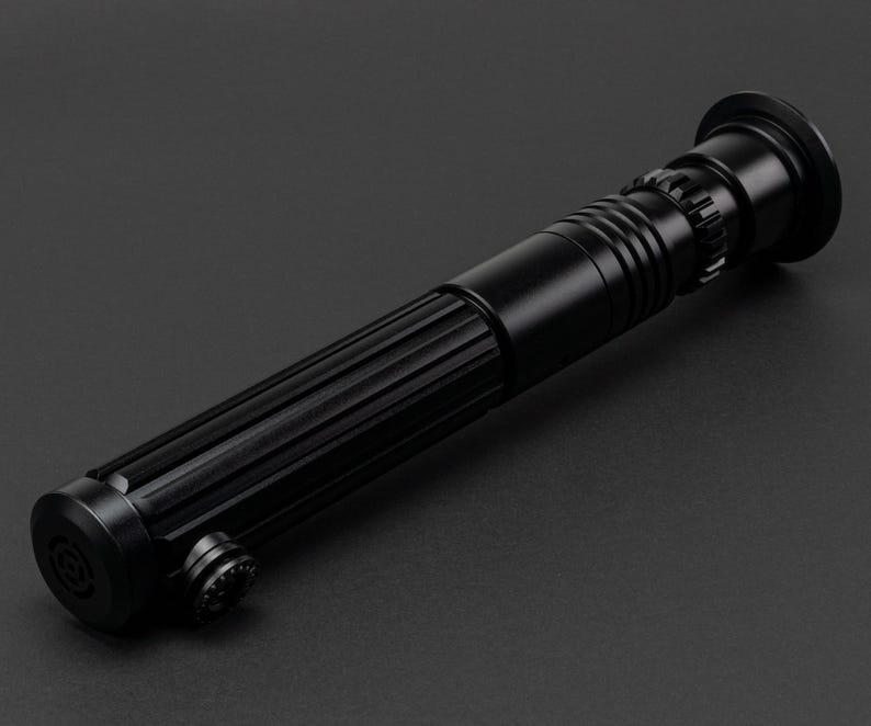 Op de afbeelding: Een zwart lightsaber-accessoire met een getextureerde handgreep en een zwarte kling.