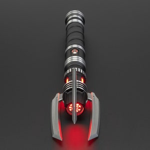 May include: A black and silver lightsaber with a red blade. The lightsaber has a unique design with a curved handle and a pointed tip.