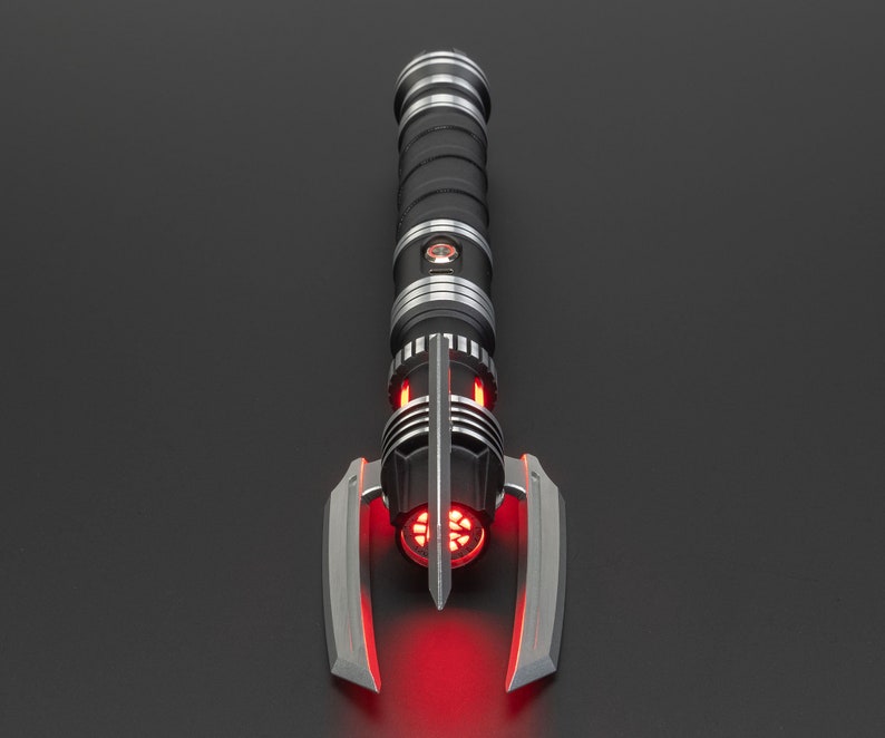 May include: A black and silver lightsaber with a red blade. The lightsaber has a unique design with a curved handle and a pointed tip.