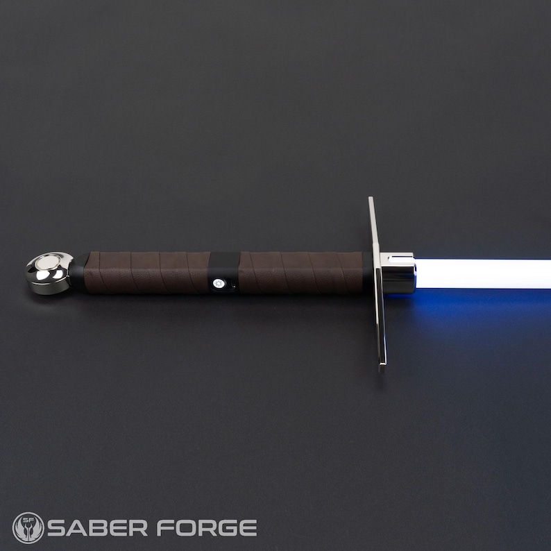 May include: A light-up sword with a brown leather-wrapped grip, a polished silver pommel, and a crossguard. The hilt features a small circular power button, and the blade emits a bright blue light. The Saber Forge logo is visible in the corner.