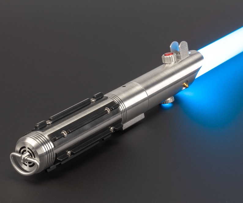 May include: A silver lightsaber with a bright blue blade extending from the top. The hilt is metallic with black accents and a red button. The lightsaber is a prop or toy, likely for cosplay or display.
