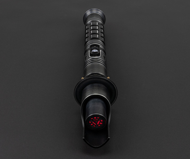 K&ouml;nnte beinhalten: Ein schwarzes Lichtschwert mit einer roten Klinge. Das Lichtschwert hat einen schwarzen Griff mit einem silbernen Knopf und einen schwarzen Emitter.