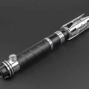 May include: A silver and black lightsaber with a textured black handle and a silver emitter with a detailed design.