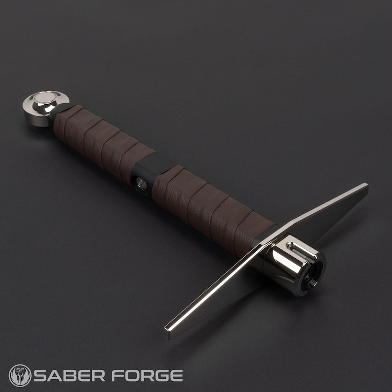 May include: A lightsaber hilt featuring a brown leather-wrapped grip, a polished silver pommel, and a crossguard with two extended silver metal quillons. The hilt includes a black control box section with a circular button and a silver emitter.