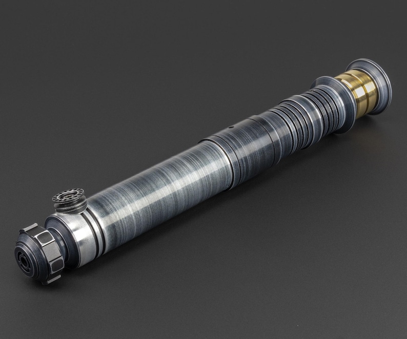 Puede incluir: Un sable de luz plateado y negro con un acento dorado en el extremo. El sable de luz tiene una superficie texturizada y un dise&ntilde;o detallado.