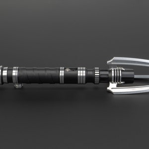 May include: A black lightsaber with silver accents and a triple-pronged blade. The lightsaber has a textured grip and a silver button on the side.