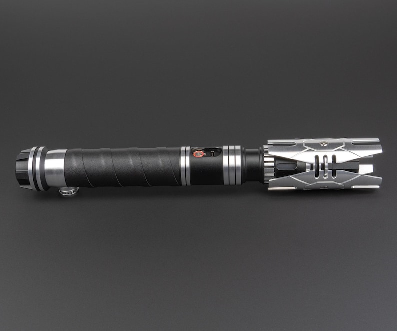 May include: A black lightsaber with a silver and black hilt. The hilt has a textured grip and a silver emitter.