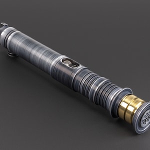 Puede incluir: Un sable de luz plateado y negro con un acento dorado. El sable de luz tiene una superficie texturizada y un dise&ntilde;o detallado.