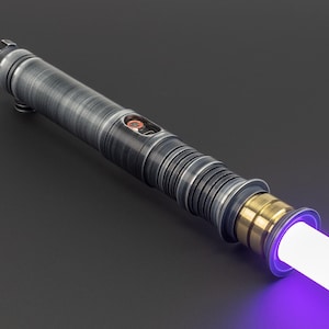 Puede incluir: Un sable de luz con una empu&ntilde;adura plateada y negra y una hoja morada. La empu&ntilde;adura tiene un acento dorado cerca de la hoja.