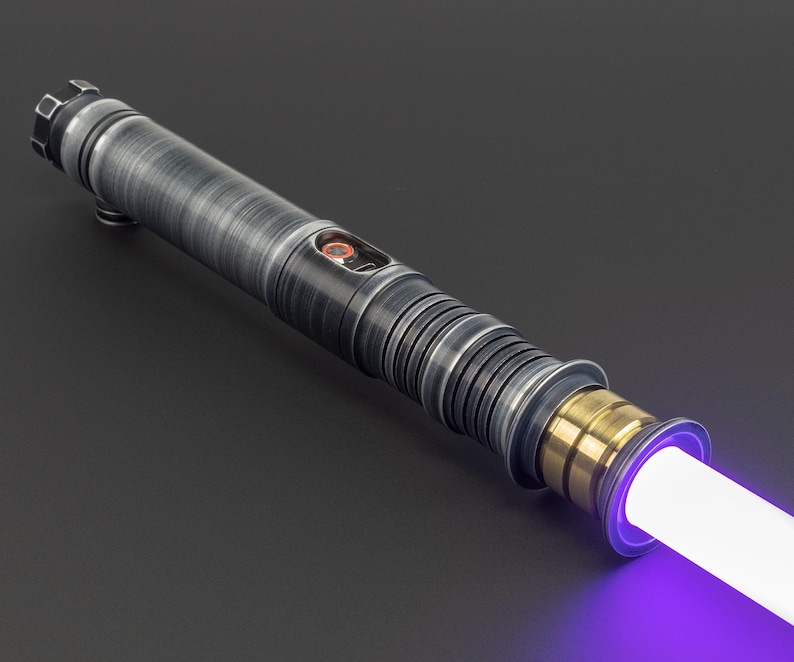 Puede incluir: Un sable de luz con una empu&ntilde;adura plateada y negra y una hoja morada. La empu&ntilde;adura tiene un acento dorado cerca de la hoja.