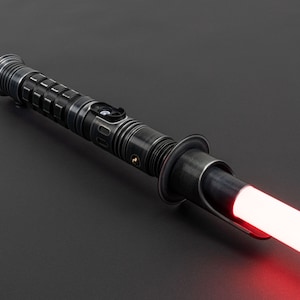 K&ouml;nnte beinhalten: Ein schwarzes Lichtschwert mit einer roten Klinge. Das Lichtschwert hat einen strukturierten Metallgriff mit einem silbernen Knopf.