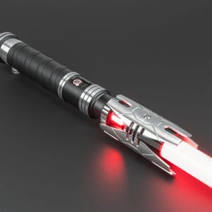 May include: A black and silver lightsaber with a red blade. The lightsaber has a textured grip and a silver emitter with a red LED light.