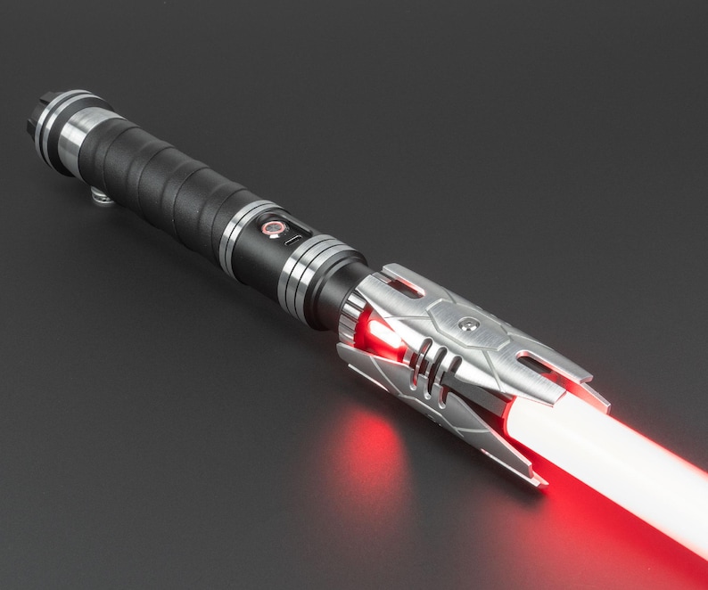 May include: A black and silver lightsaber with a red blade. The lightsaber has a textured grip and a silver emitter with a red LED light.