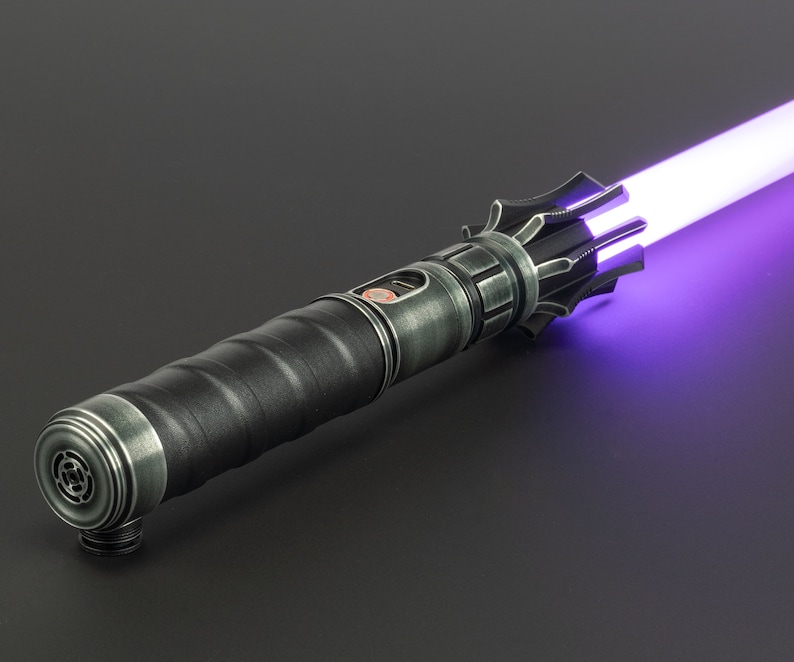 K&ouml;nnte beinhalten: Ein schwarzes Lichtschwert mit einer violetten Klinge. Das Lichtschwert hat einen strukturierten Griff und eine silberne Akzentuierung in der N&auml;he der Klinge.