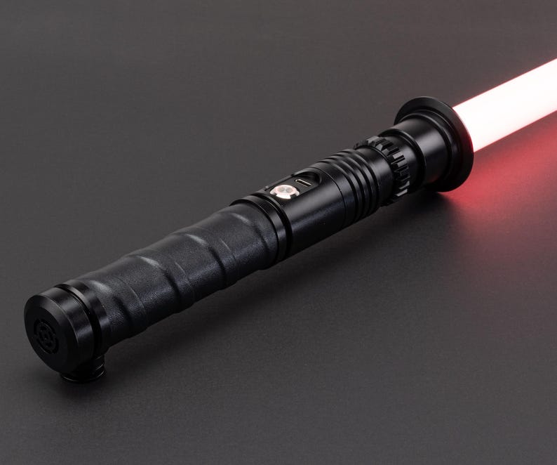 May include: A black lightsaber with a red blade. The lightsaber has a textured grip and a black emitter.