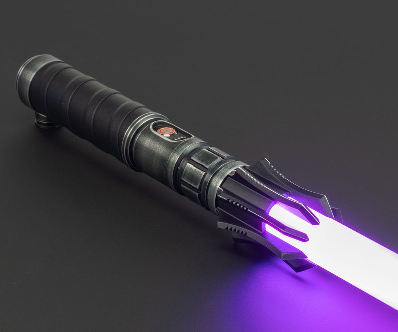 K&ouml;nnte beinhalten: Ein schwarzes Lichtschwert mit einer violetten Klinge. Das Lichtschwert hat einen strukturierten schwarzen Griff mit einem silbernen Akzent und einen schwarzen Emitter mit einem silbernen Ring.