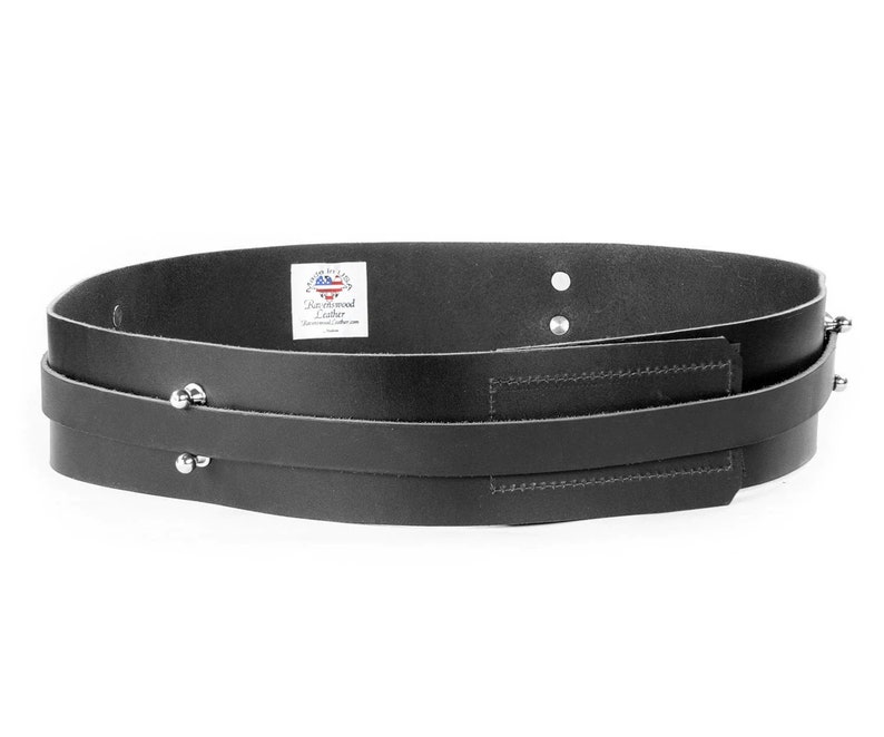 Puede incluir: Cintur&oacute;n de cuero negro con dos correas y tachuelas plateadas. El cintur&oacute;n tiene un peque&ntilde;o bolsillo rectangular en la parte delantera. La etiqueta dice "Cuero hecho a mano".