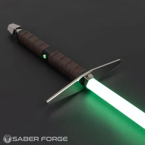 Op de afbeelding: Een lightsaber met een groene blade en een bruine leren grip. Het handvat is zilver en heeft een zwarte accent. De lightsaber is op een donkergrijze achtergrond. SABER FORGE is in wit gedrukt aan de onderkant van de afbeelding.