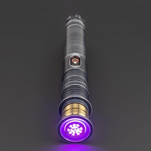 Puede incluir: Un sable de luz plateado con una hoja morada y un acento dorado. El sable de luz tiene un emisor circular con un s&iacute;mbolo en el centro.