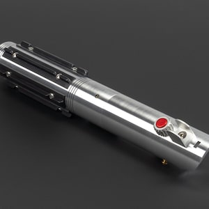 May include: A silver lightsaber with black accents and a red button. The hilt features a ribbed design and a curved end. The lightsaber is a prop or collectible item.