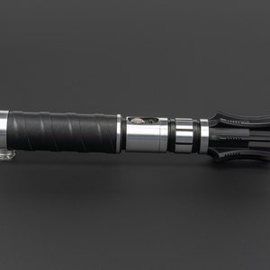 May include: A black and silver lightsaber with a unique, multi-pronged blade design. The hilt features a textured grip and a silver metal band.