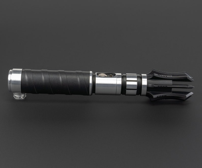 May include: A black and silver lightsaber with a unique, multi-pronged blade design. The hilt features a textured grip and a silver metal band.