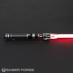 Puede incluir: Un sable de luz negro y plateado con una hoja roja. El sable de luz tiene un agarre texturizado y un emisor plateado.